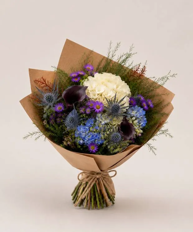 Signature wrapped bouquet with white hydrangea, blue and purple blooms in kraft paper
